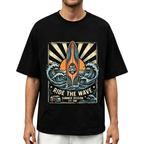 A man wearing a black short-sleeve t-shirt with a large vintage-style graphic on the chest featuring a surfboard, ocean waves, and the text 'WEST COAST CO' and 'RIDE THE WAVE'.