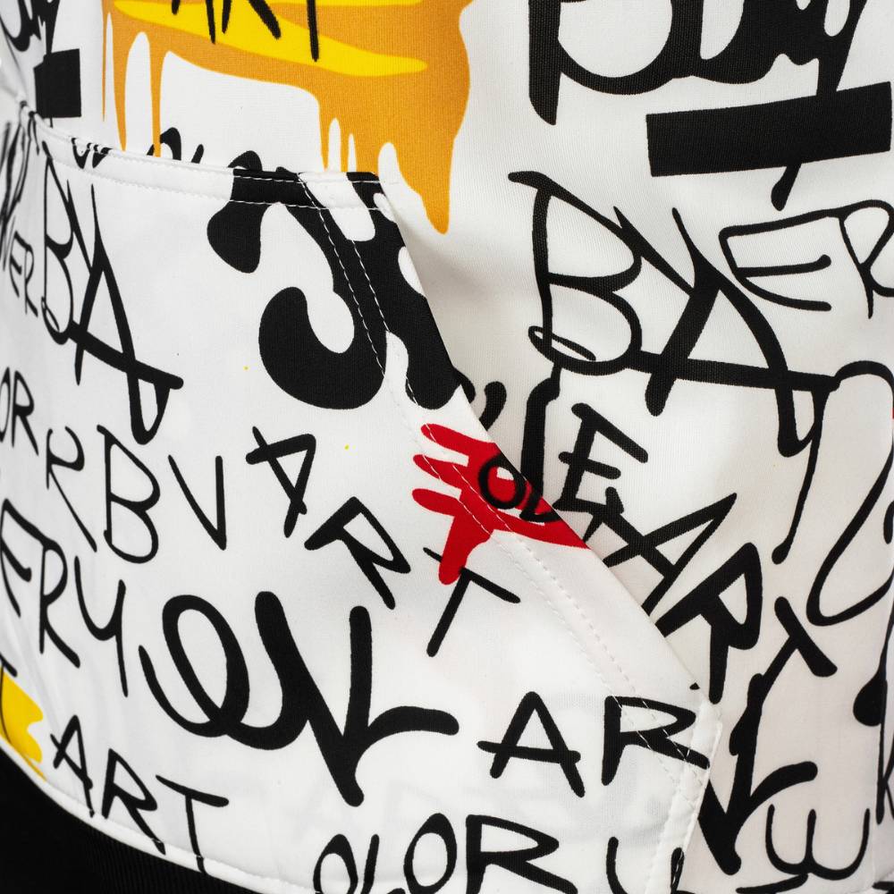 Close-up of a white garment covered in black graffiti-style lettering and paint-drip graphics, with a small red hand logo near the center.