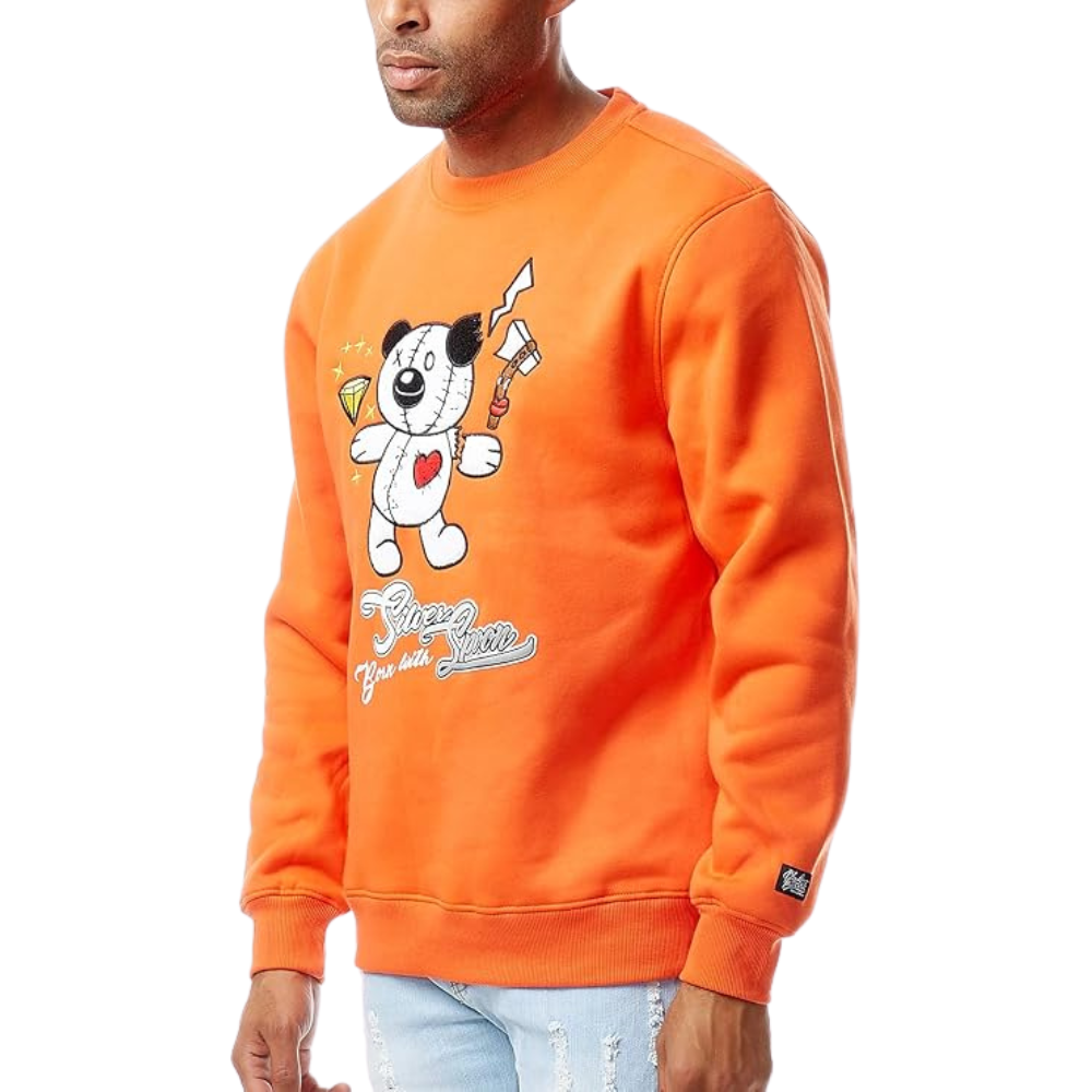 A man wearing a bright orange crewneck sweatshirt featuring a cartoon dog graphic holding a paintbrush with 'Creative Dogs' text below it, paired with light blue jeans against a white background.