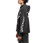 A side-profile view of a person wearing a faded black pullover hoodie with a large white tribal graphic printed down the sleeve and across the back, paired with dark jeans against a plain white background.