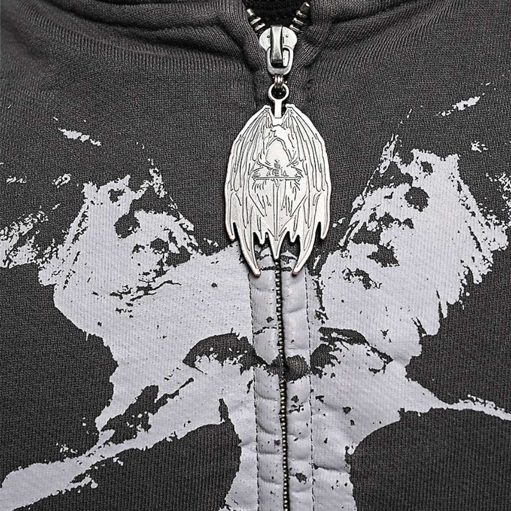 Close-up of a black zip-up hoodie with a distressed gray graphic print and a highly detailed silver metal zipper pull featuring a winged skull design.