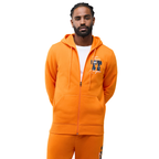 A man wearing a bright orange zip-up hoodie and matching orange sweatpants, featuring a graphic print on the left chest, against a plain white background.