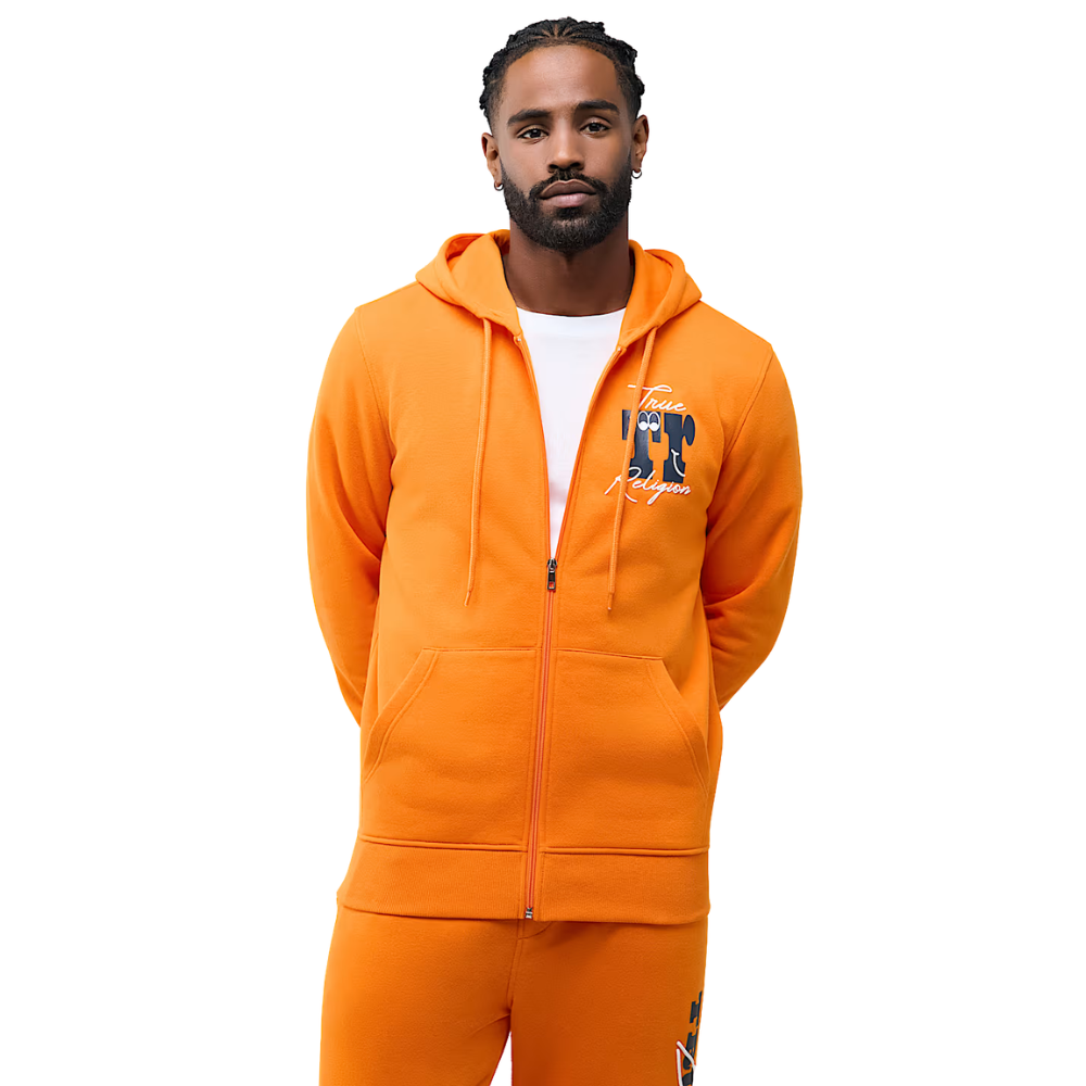 A man wearing a bright orange zip-up hoodie and matching orange sweatpants, featuring a graphic print on the left chest, against a plain white background.