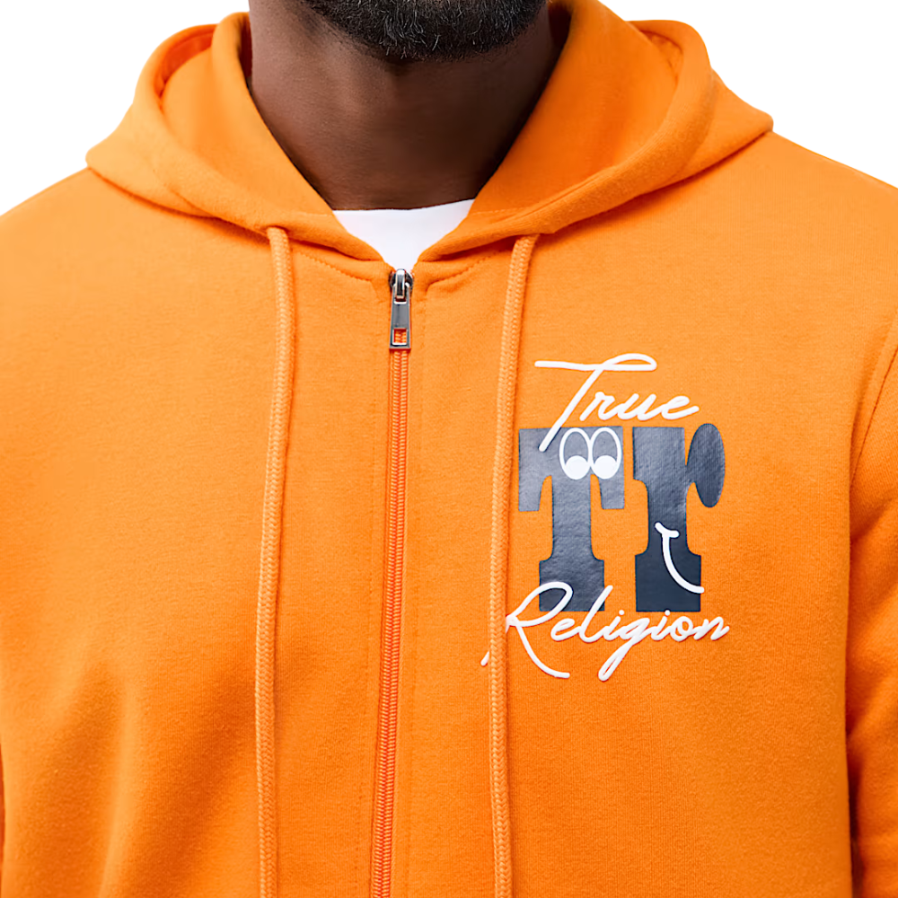 Close-up of a person wearing a bright orange zip-up hoodie with a front graphic that reads 'True TT Religion' in white and dark blue, over a white undershirt.